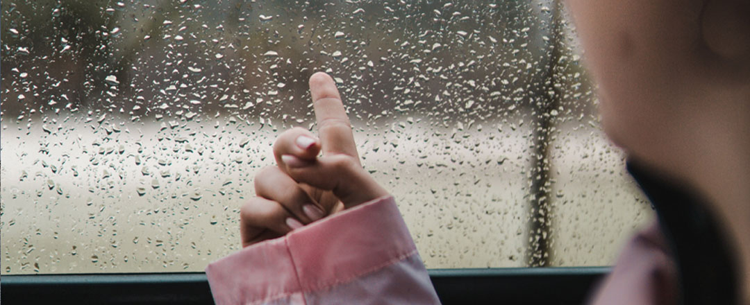 menina apontando de dentro do ônibus para algum ponto em um dia chuvoso
