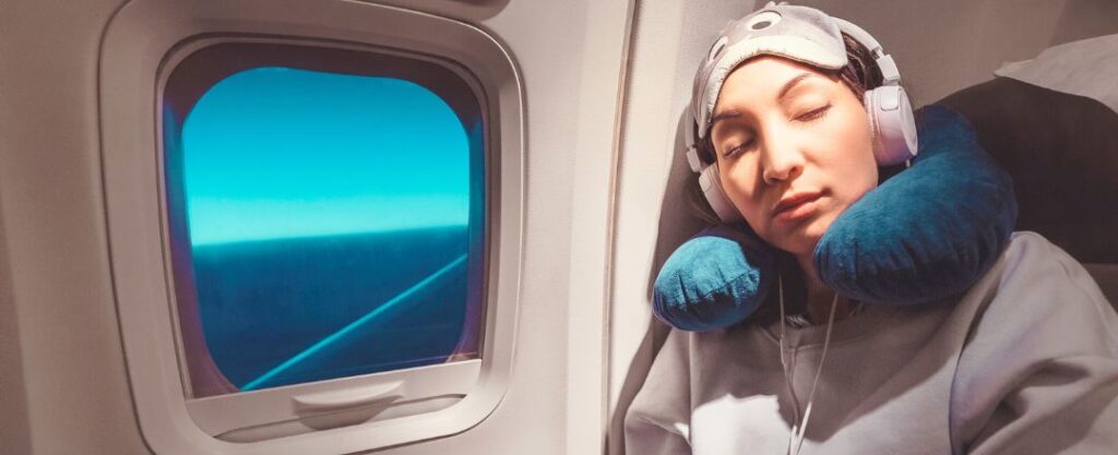 Mulher dormindo em um avião com fones de ouvido e travesseiro de pescoço