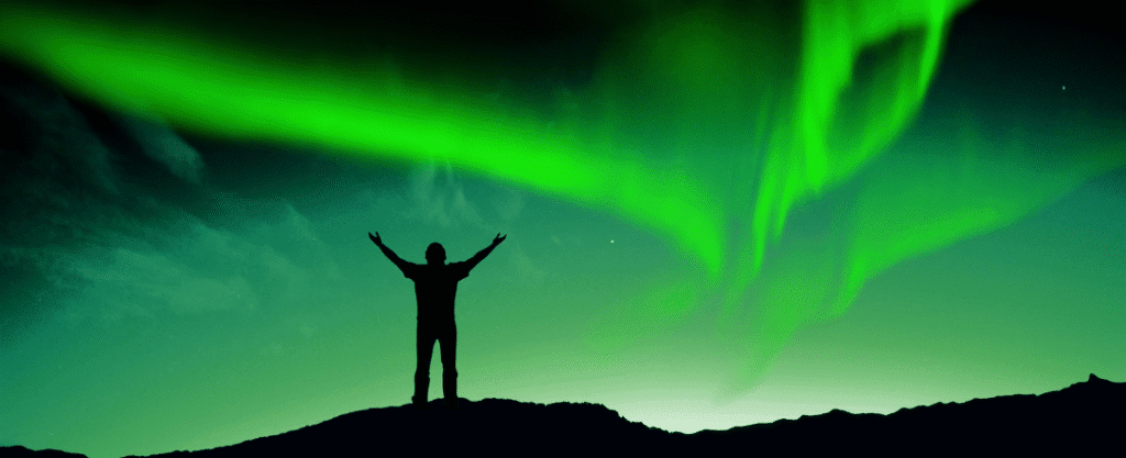 homem de braços abertos saudando a aurora boreal